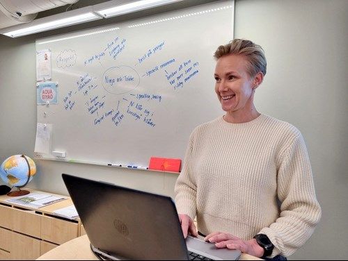 Leende kvinna vid dator med whiteboard i bakgrunden